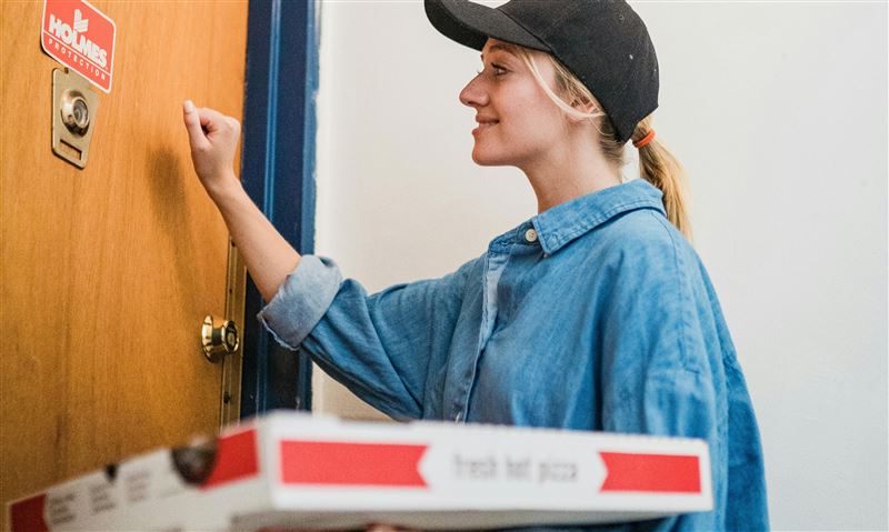 A friendly courier knocking on a door with a fresh pizza